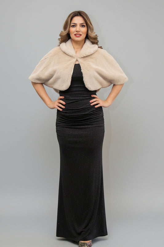 Woman in a black dress with a beige fur shrug standing in front of a mirror.