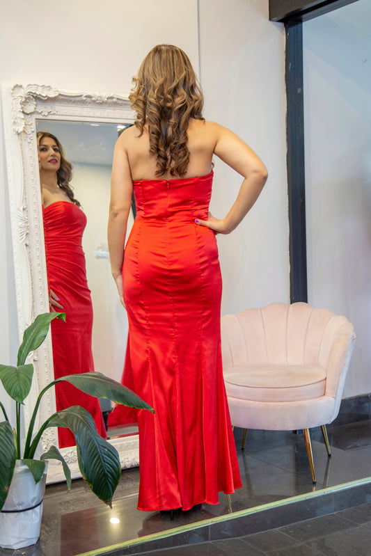 Woman in a red strapless gown standing in front of a mirror.
