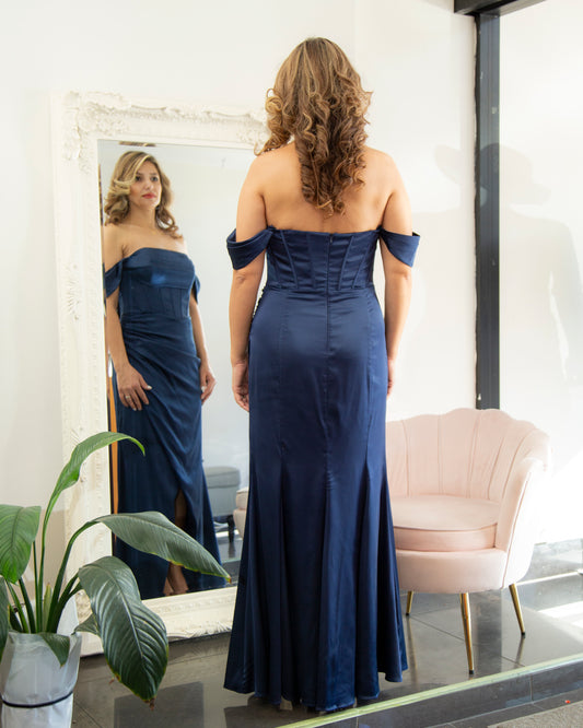 Woman in a navy off-shoulder gown standing in front of a mirror.