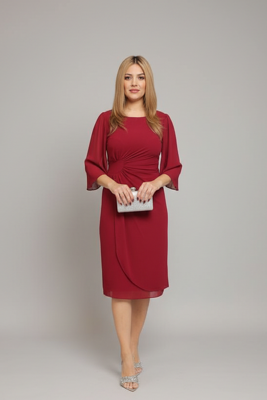 A woman modeling a knee-length red dress with elbow-length sleeves and a draped wrap-style front, holding a small white clutch against a plain light gray studio background.