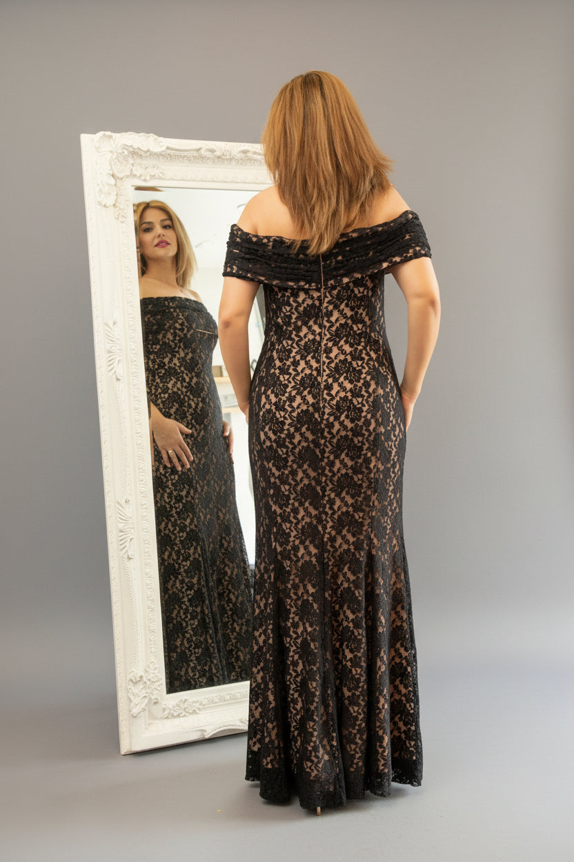 Woman in a black lace off-shoulder gown standing in front of a mirror.