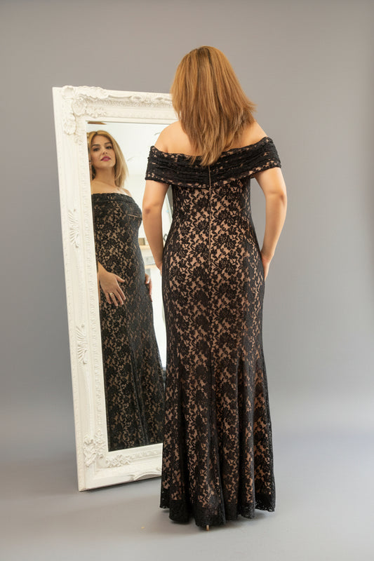 Woman in a black lace off-shoulder gown standing in front of a mirror.