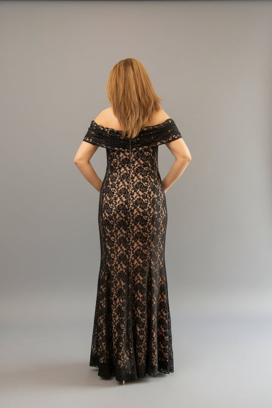Woman in a black lace off-shoulder gown standing in front of a mirror.