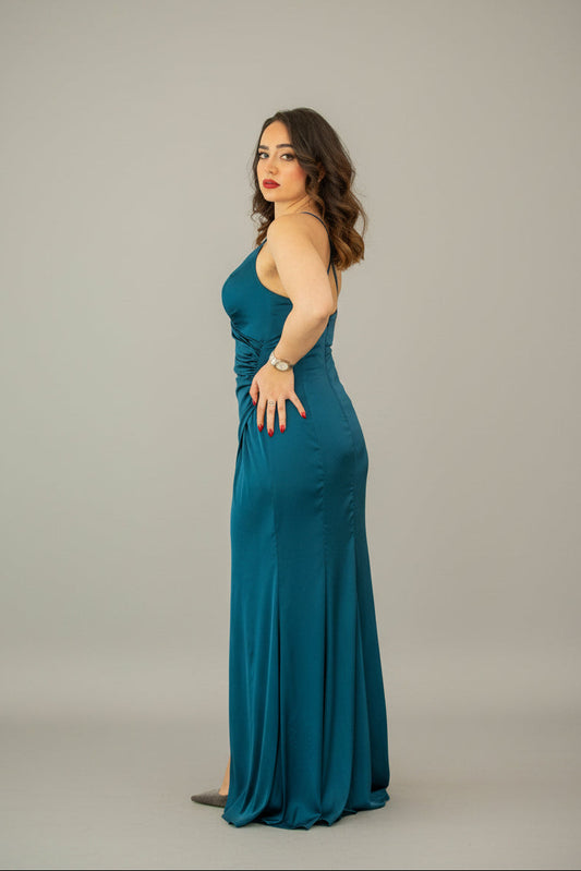 Woman in a teal evening gown standing against a white wall with decorative lamps.