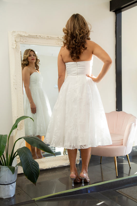 Woman trying on a white dress in front of a mirror.