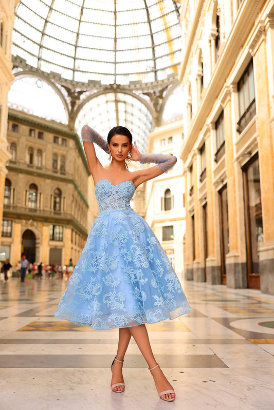 Woman in a light blue dress standing in an elegant indoor setting with architectural columns.