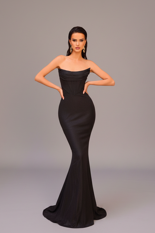 A woman modeling a strapless black mermaid gown with a fitted bodice and flared skirt, standing against a plain light gray studio background.