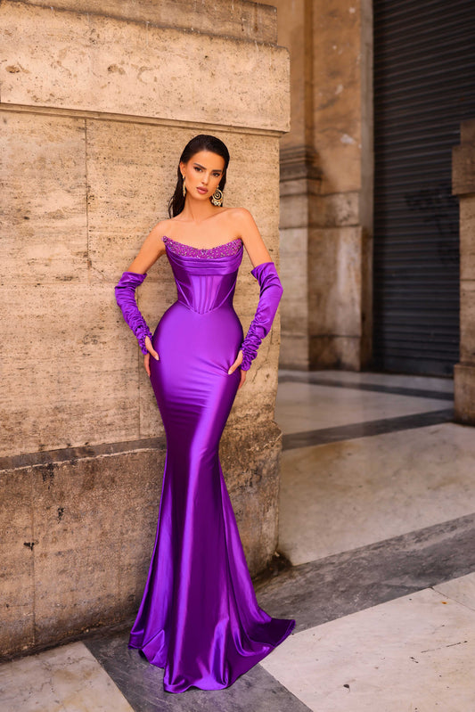 Woman in a purple evening gown and gloves standing against a stone wall.