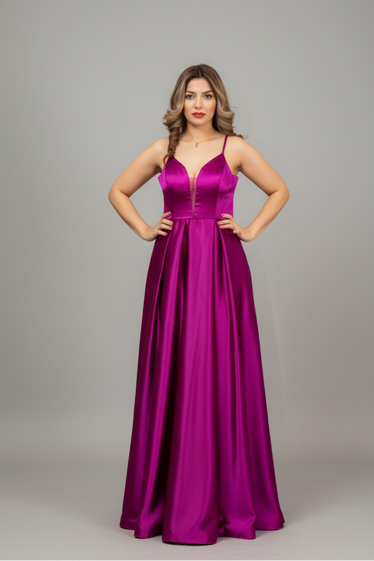 A woman modeling a floor-length magenta satin gown with spaghetti straps and a V-neckline, standing against a solid gray studio background.
