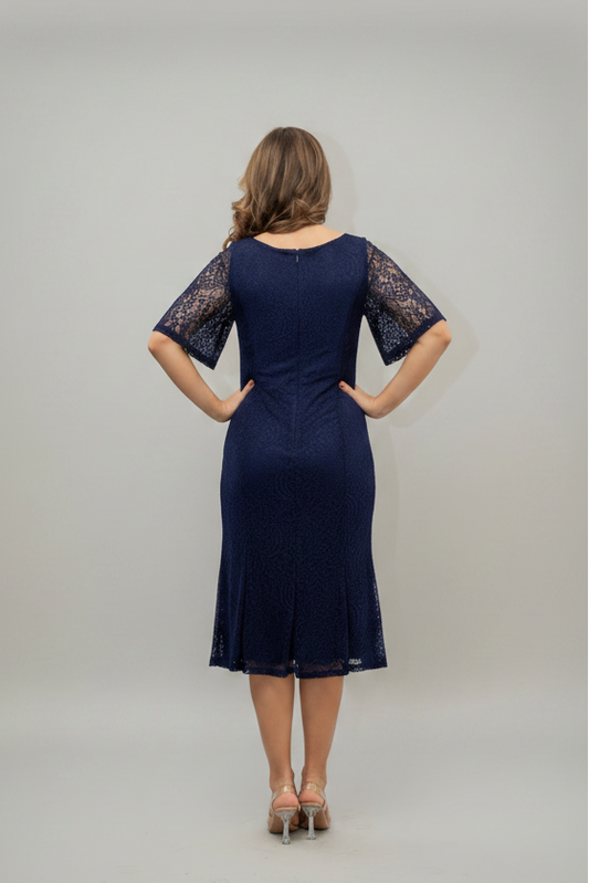 A woman viewed from the back wearing a navy blue knee-length dress with lace short sleeves and a lace hem, standing against a light gray studio background.