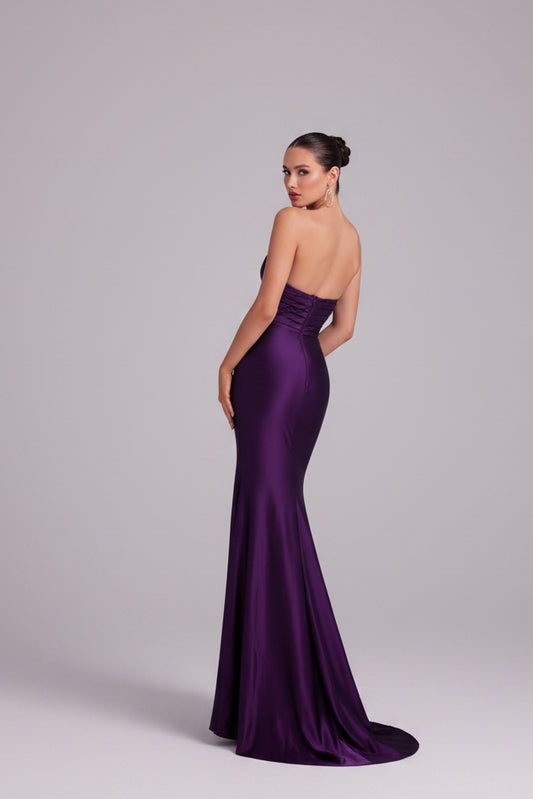 Woman in a purple gown standing next to a white angel statue on a balcony.