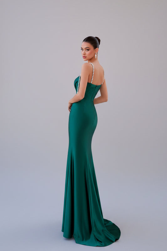 Woman in a green evening gown standing on a balcony with classical columns.