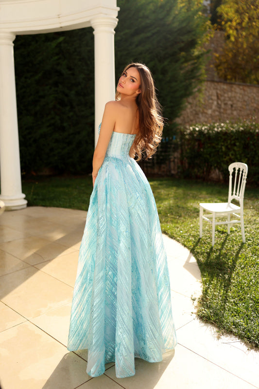 Woman in a light blue strapless gown standing outdoors near a white columned structure.
