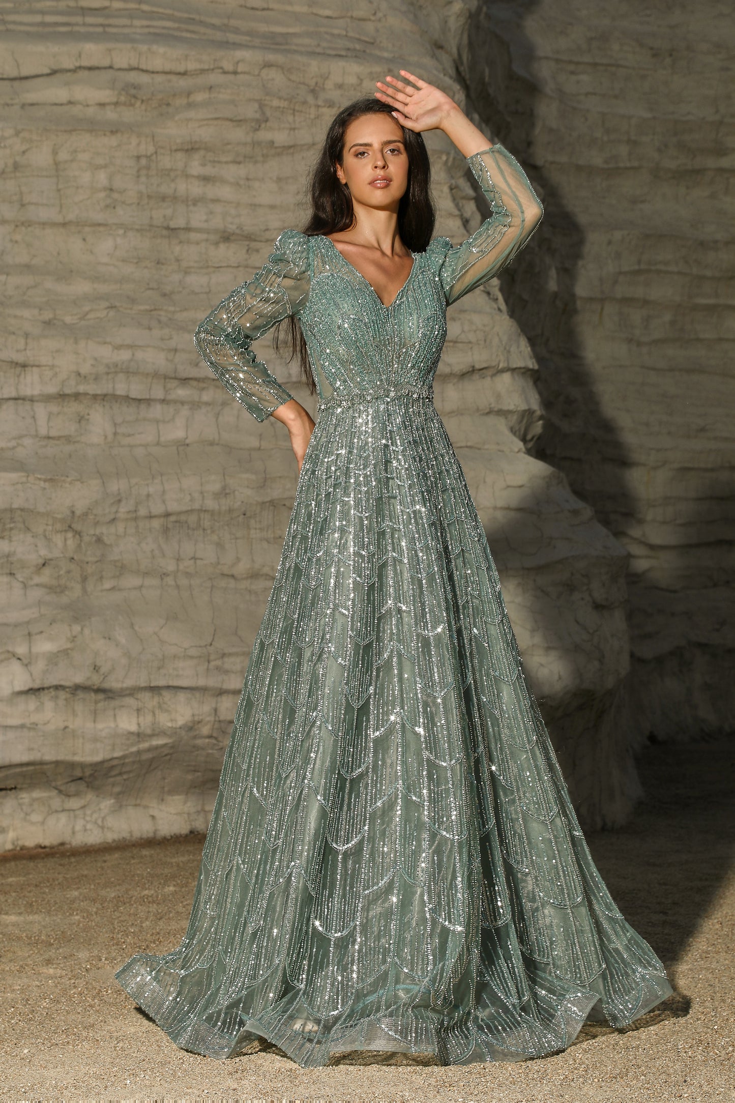 Woman in a long, sparkly green dress standing against a textured stone wall.