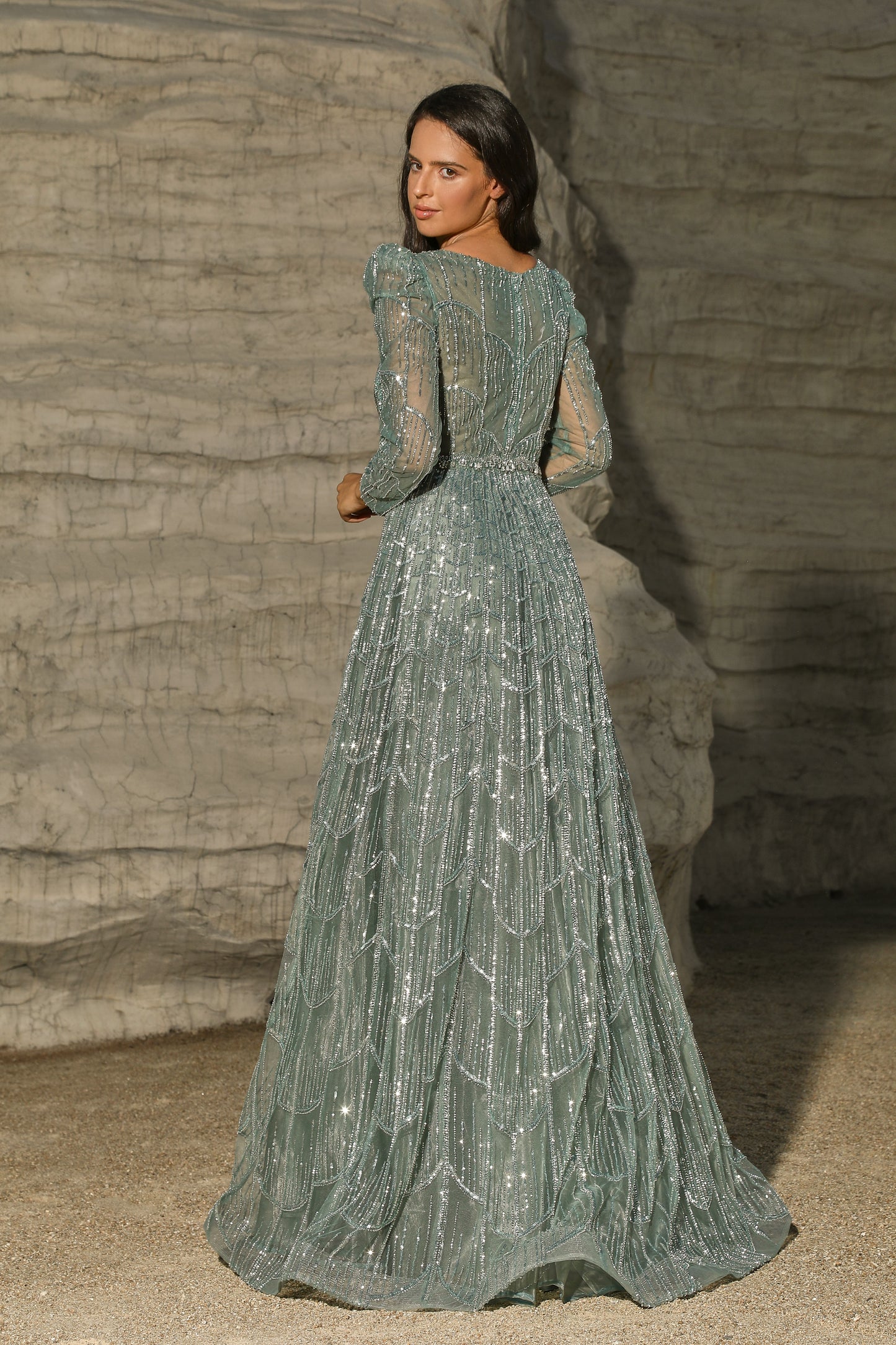 Woman in a long, elegant green dress standing against a textured stone wall.