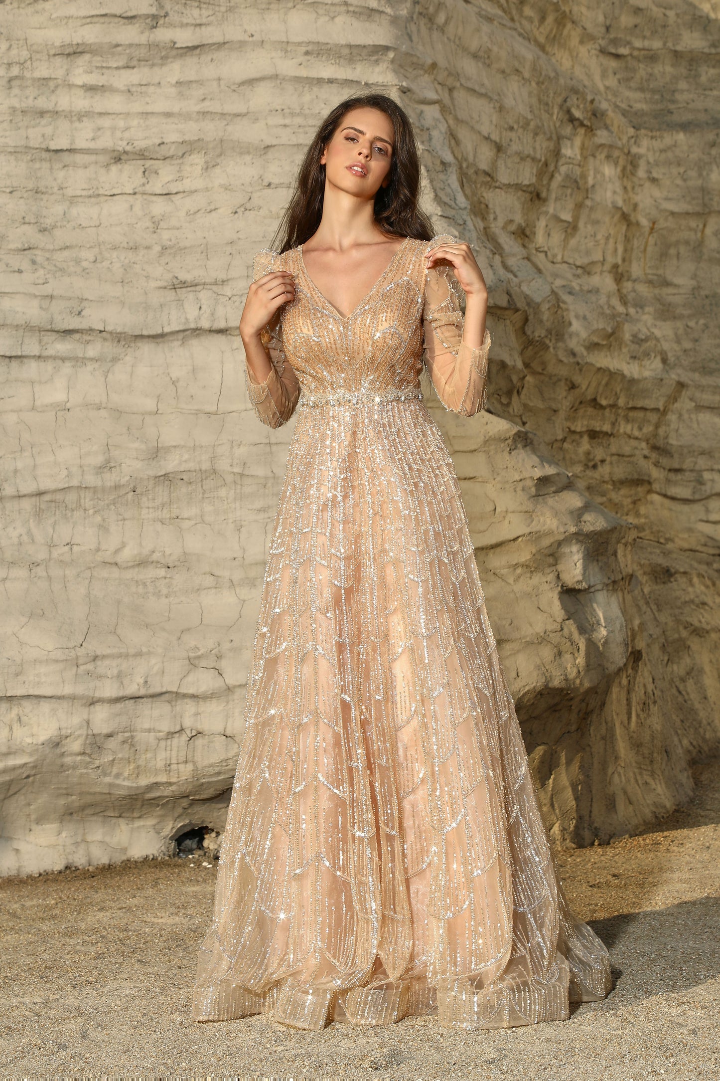 Woman in a long, elegant dress standing against a rocky cliff.