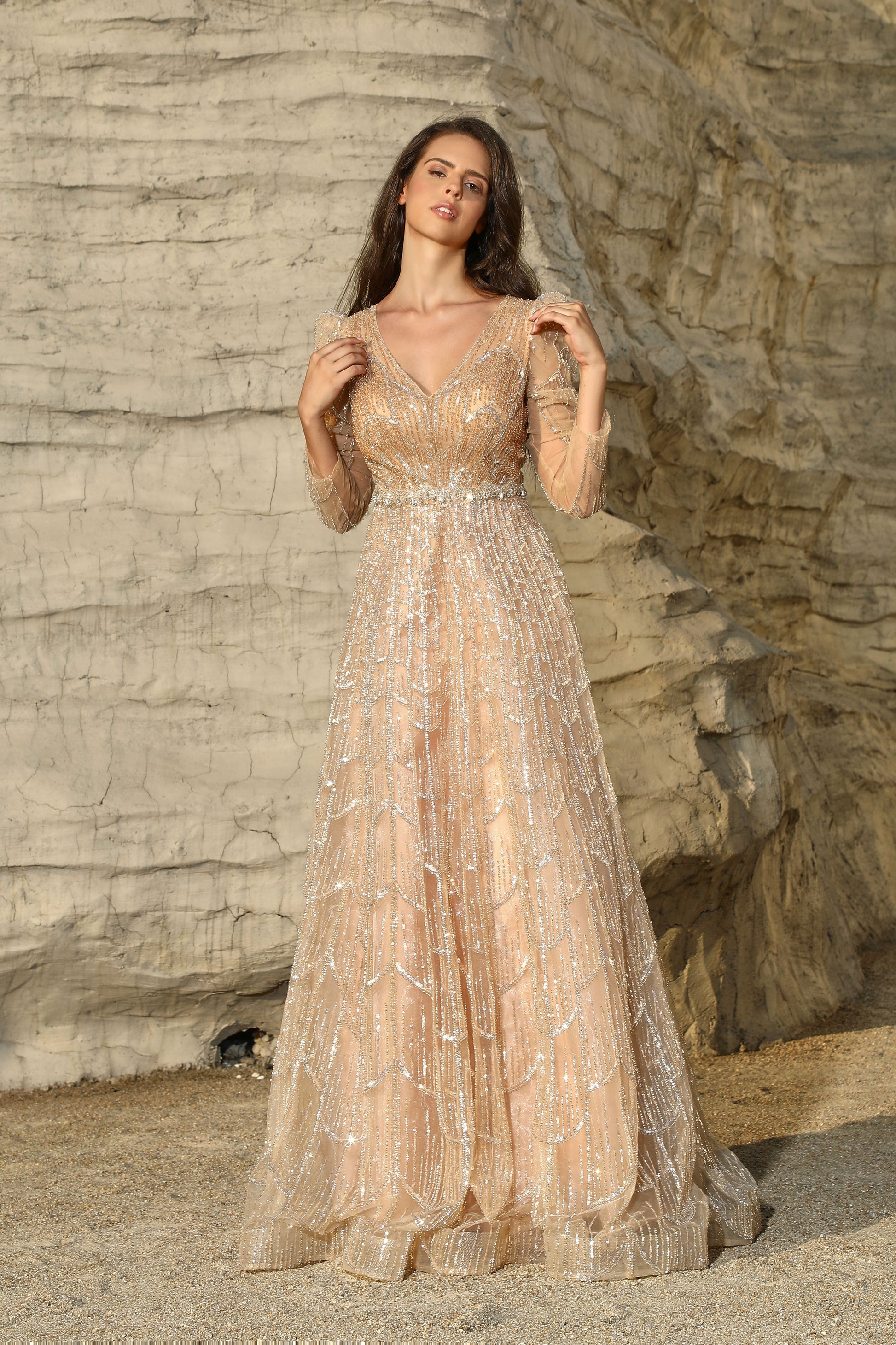 Woman in a long, elegant dress standing against a rocky cliff.