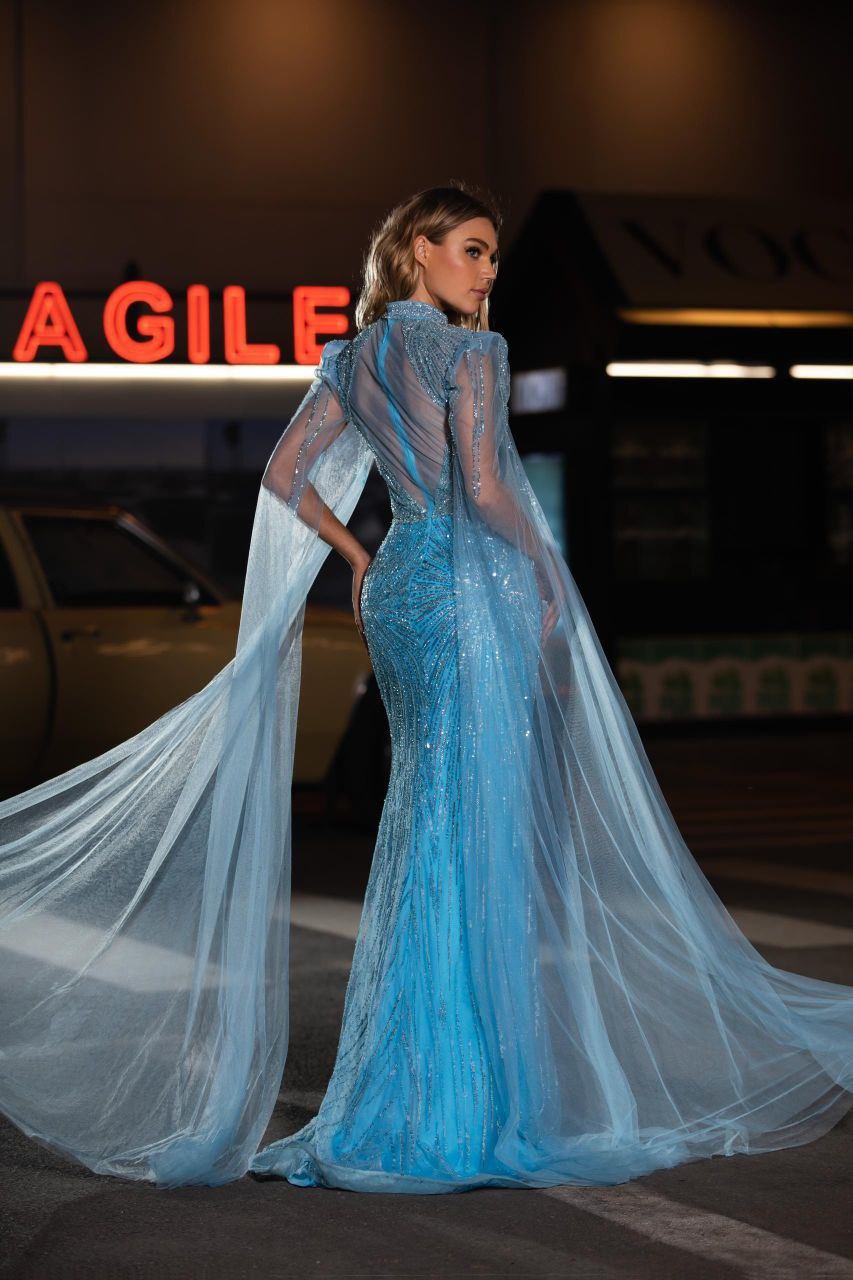 Woman in a blue evening gown with a long train standing.
