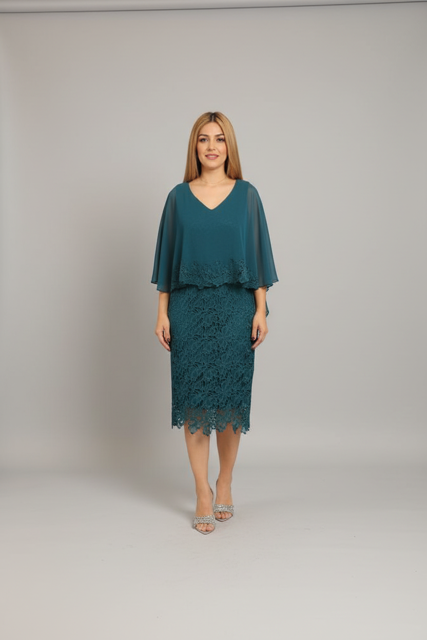 A woman modeling a teal blue-green lace midi dress with sheer flutter sleeves, standing in a boutique next to a pink shell chair.
