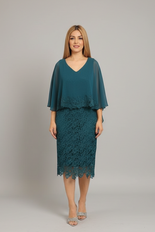 A woman modeling a teal blue-green lace midi dress with sheer flutter sleeves, standing in a boutique next to a pink shell chair.