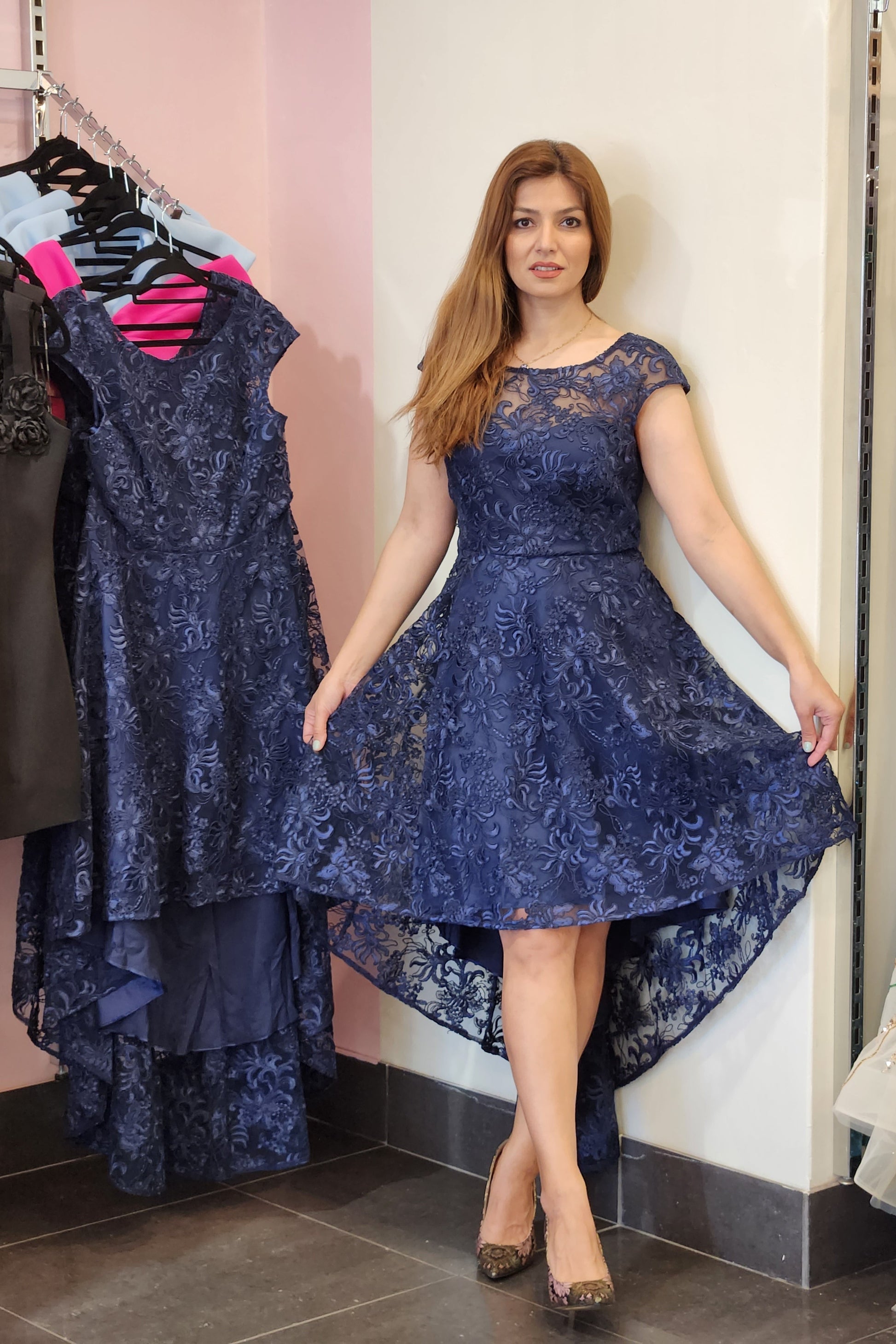 Woman holding a blue lace dress in a fitting room.