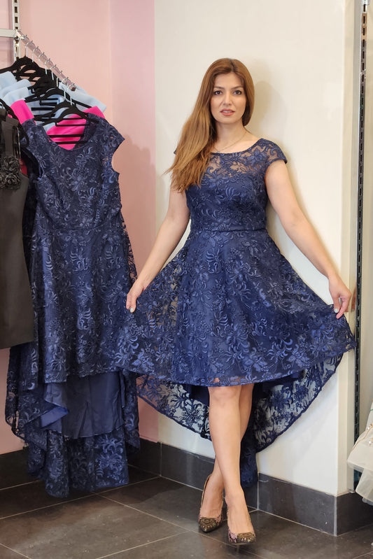 Woman holding a blue lace dress in a fitting room.