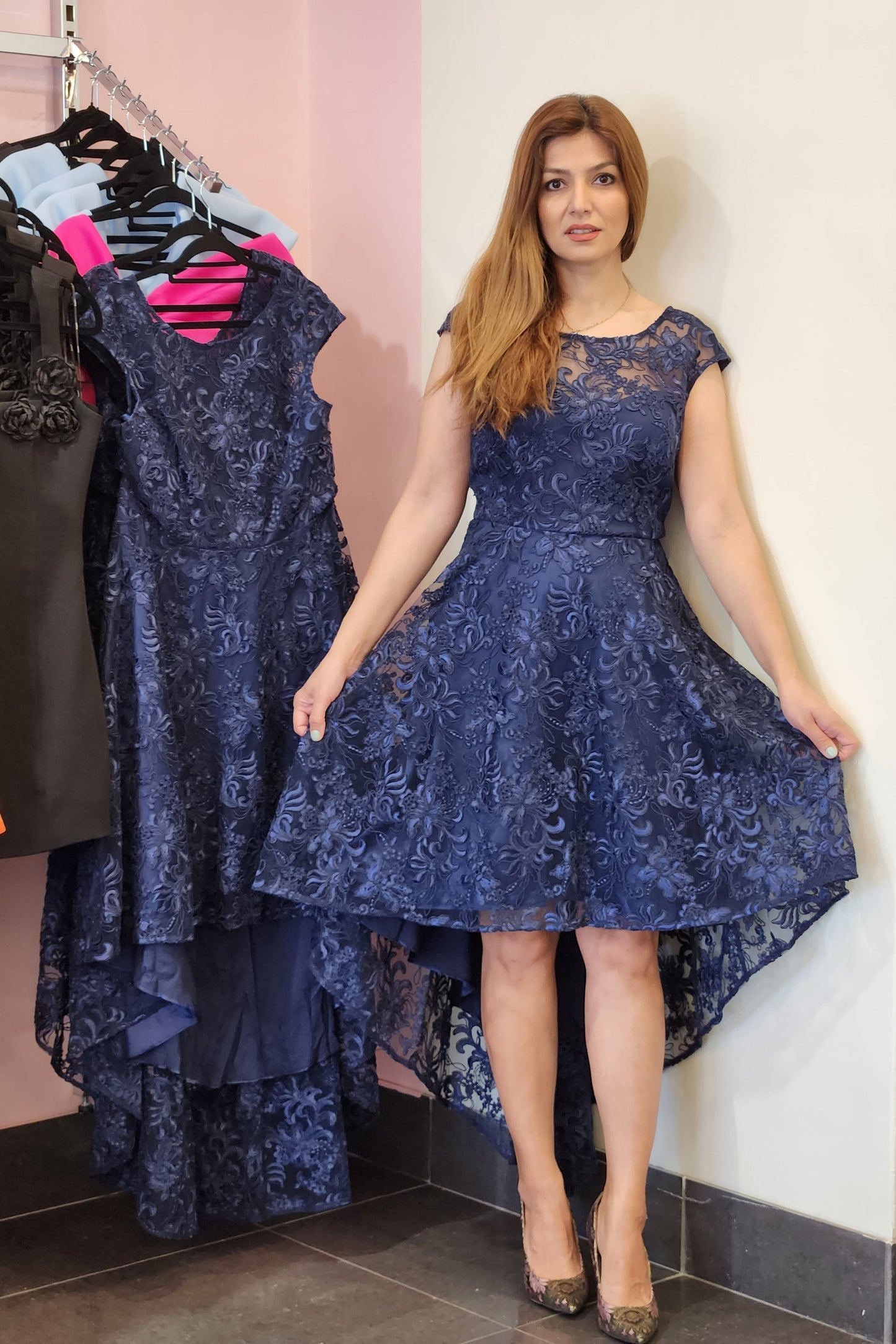 Woman holding a blue lace dress with a rack of clothes in the background