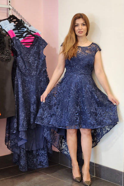 Woman holding a blue lace dress with a rack of clothes in the background