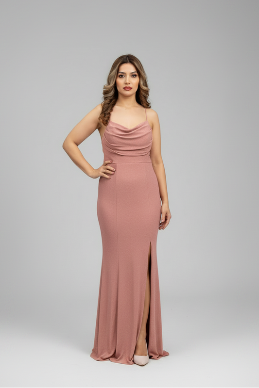 A woman modeling a floor-length dusty rose pink gown with spaghetti straps, a draped cowl neckline, a fitted silhouette, and a thigh-high front slit, photographed against a light gray studio background.