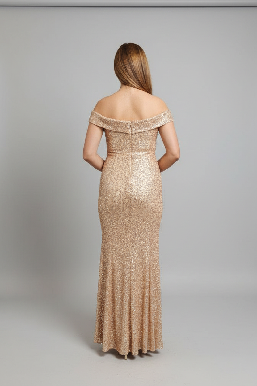 A woman viewed from the back wearing a floor-length off-the-shoulder evening gown covered in shimmering champagne sequins against a light gray studio background.