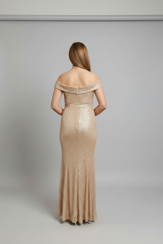 A woman viewed from the back wearing a floor-length off-the-shoulder evening gown covered in shimmering champagne sequins against a light gray studio background.