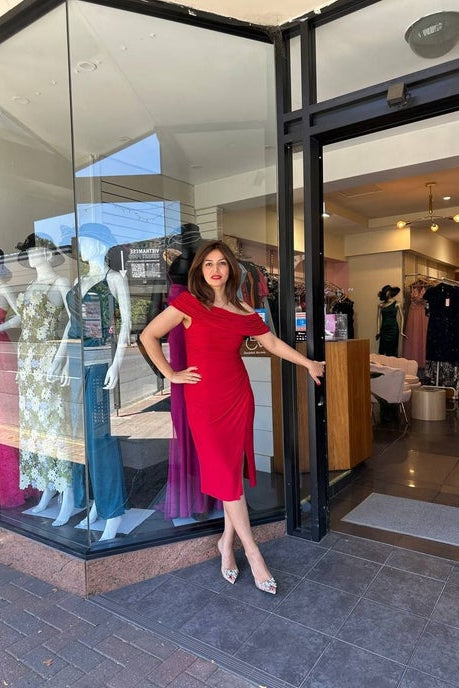 Woman in a red dress standing outside a fashion store with mannequins inside.