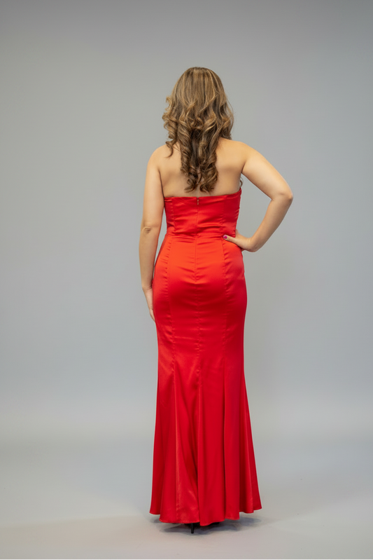 A woman modeling a strapless red floor-length gown from the back, standing against a plain light gray studio background.