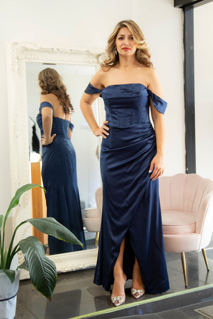 Woman in a navy blue off-shoulder gown standing in front of a mirror.