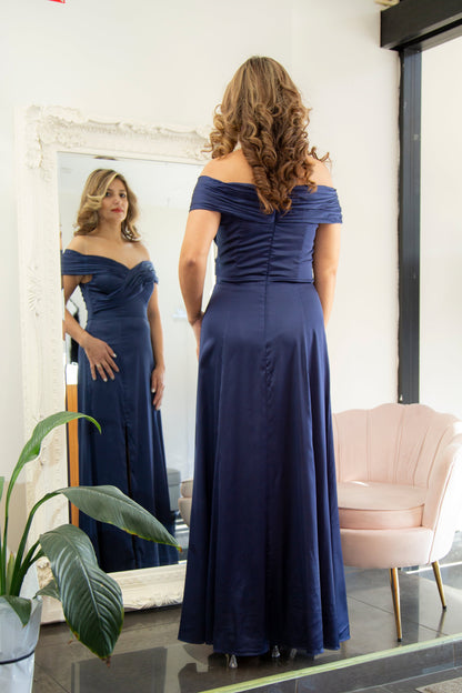 Woman in a blue off-shoulder gown standing in front of a mirror.