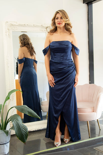 Woman in a navy blue off-shoulder gown standing in front of a mirror.
