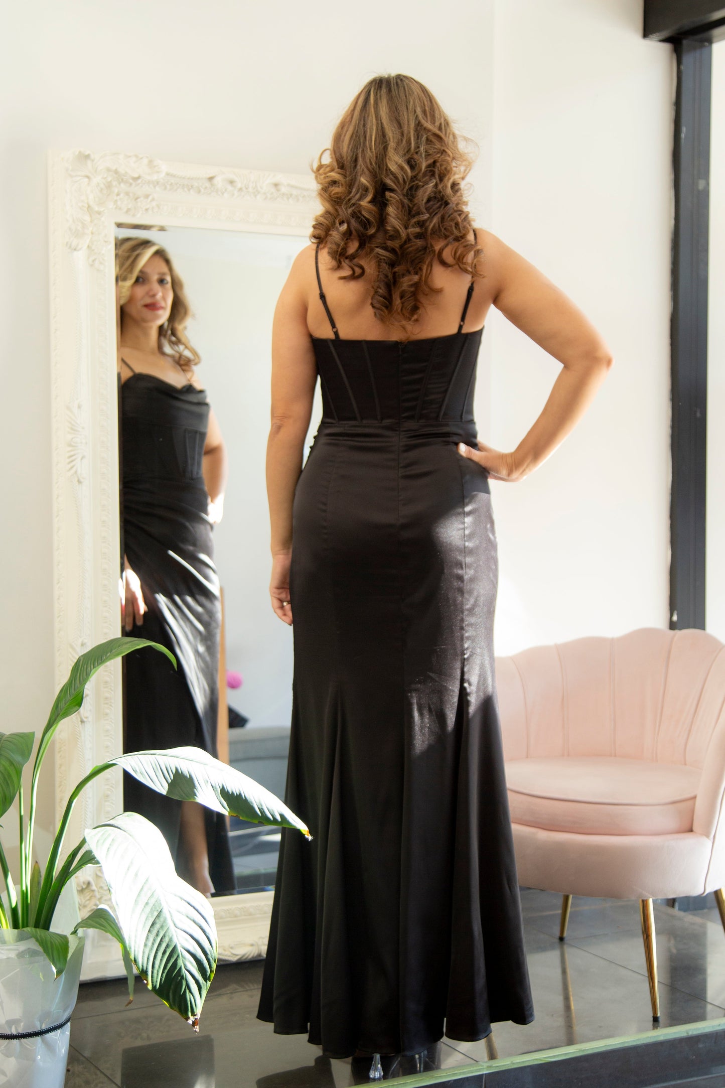 Woman in a black evening gown standing in front of a mirror.