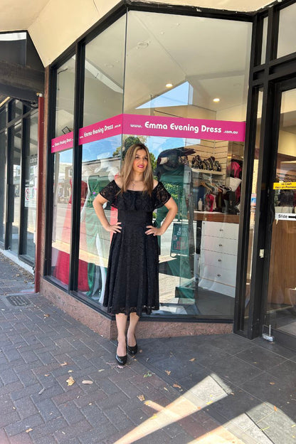 Woman in a black dress standing outside a store with a 'Emma Evening Dress' sign.