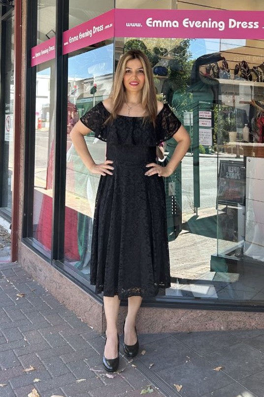 Woman in a black evening dress standing in front of a store window with 'Emma Evening Dress' branding.