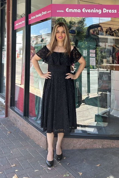 Woman in a black evening dress standing in front of a store window with 'Emma Evening Dress' branding.