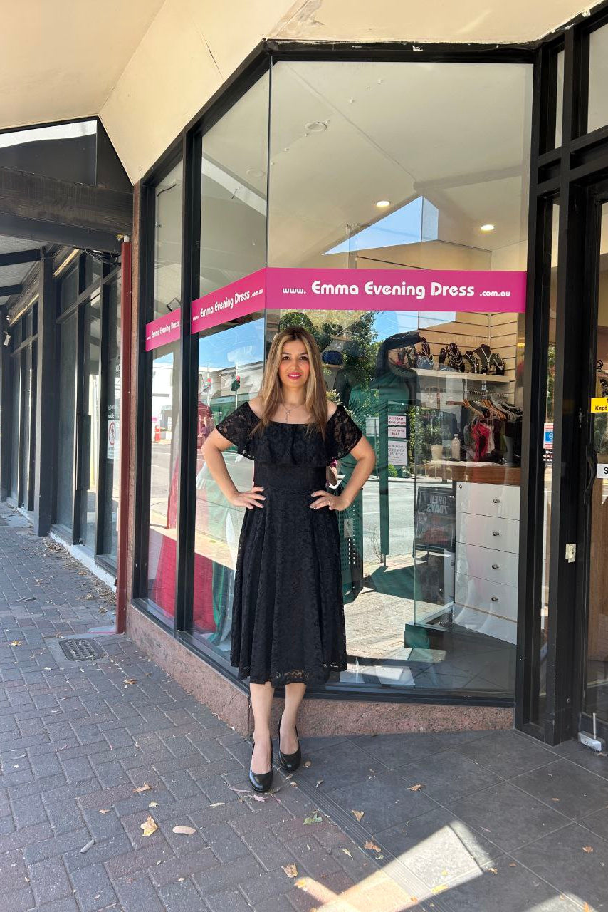 Woman in a black dress standing outside a store named 'Emma Evening Dress'.