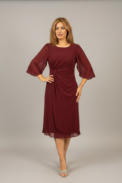 Woman wearing a red dress with sheer sleeves on a plain background