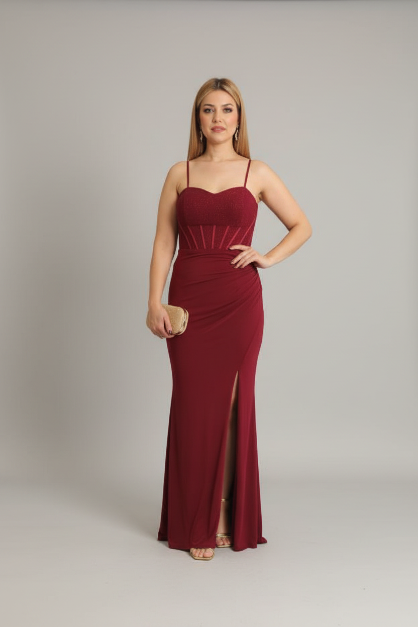 A woman modeling a floor-length burgundy maxi dress with spaghetti straps, a sweetheart neckline, a fitted silhouette, and a thigh-high front slit, standing against a light gray studio background.
