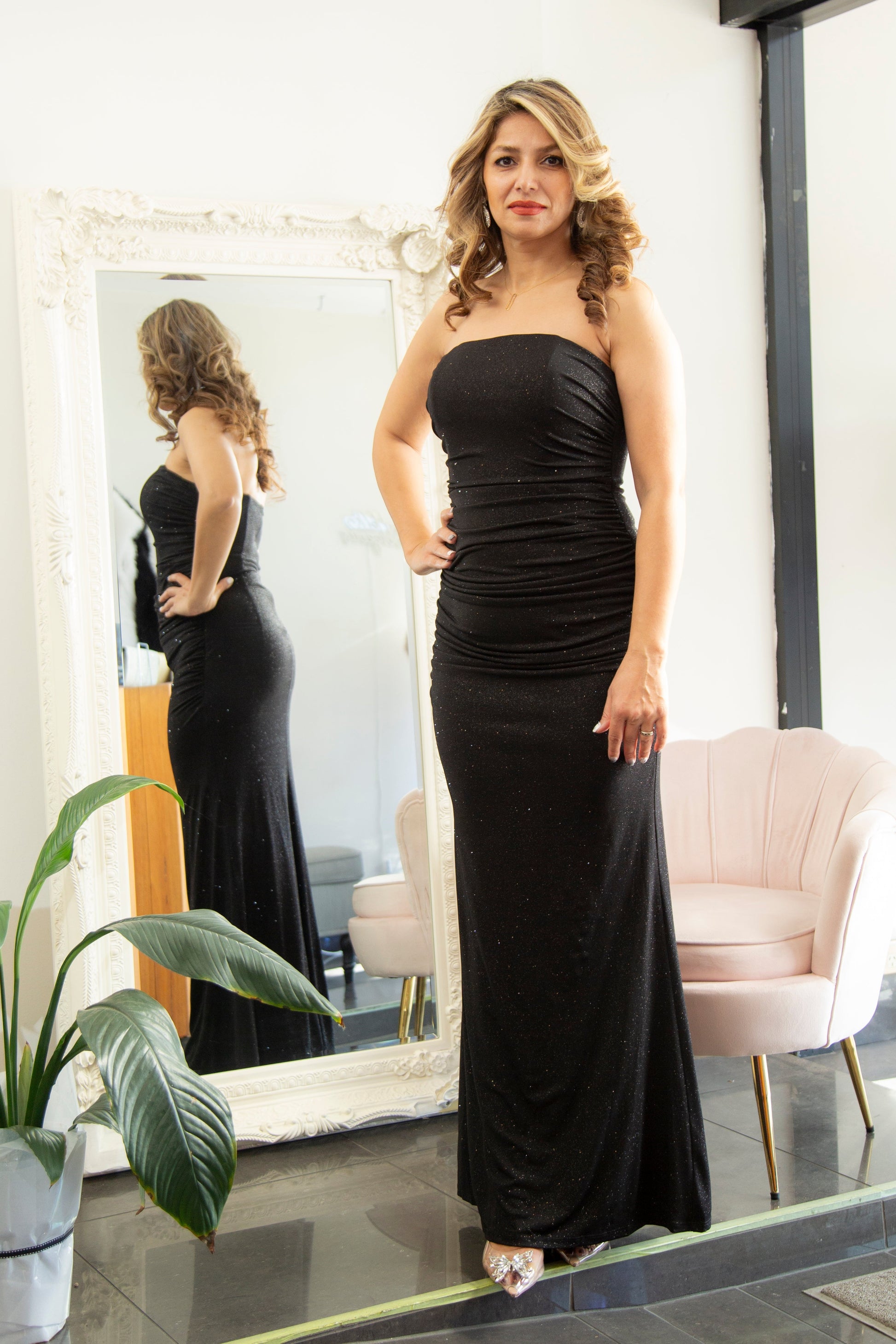 Woman in a black evening gown standing in front of a mirror.
