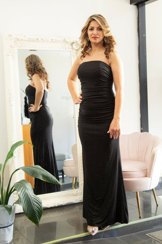 Woman in a black evening gown standing in front of a mirror.