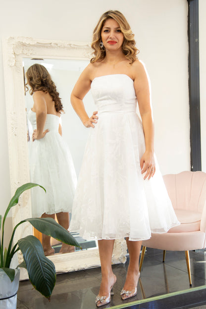 Woman trying on a white strapless dress in front of a mirror.