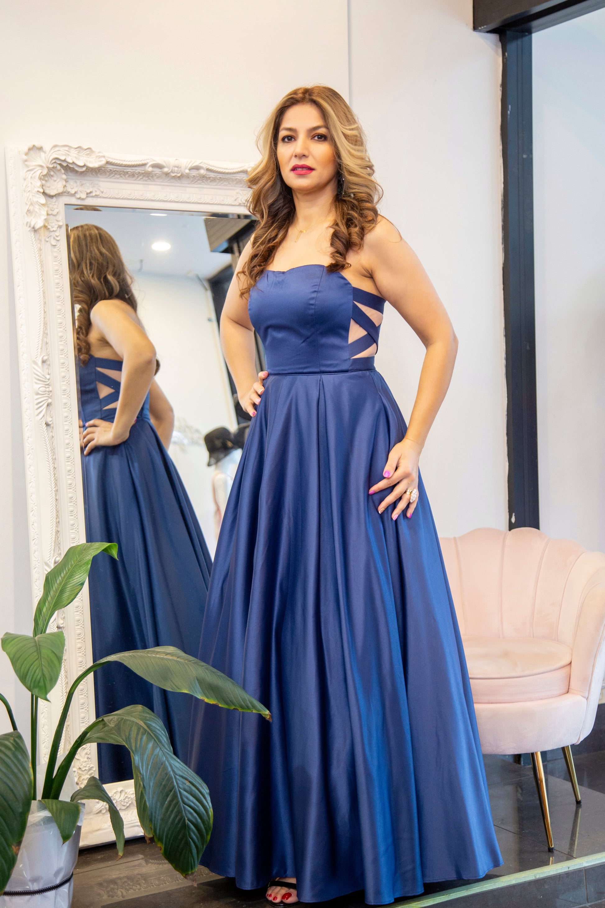 Woman in a blue evening gown standing in front of a mirror.