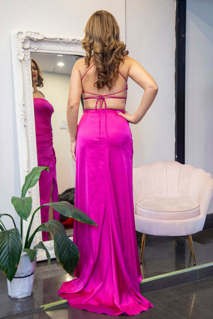Woman in a pink dress standing in front of a mirror in a room with a plant and chair.