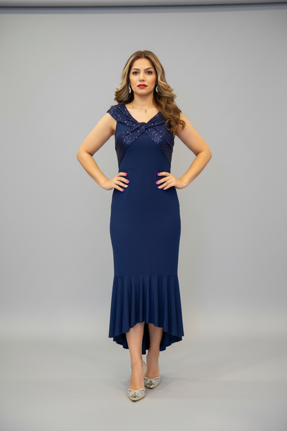 A woman modeling a navy blue high-low formal dress with a lace bodice and ruffled hem, standing against a light gray studio background.