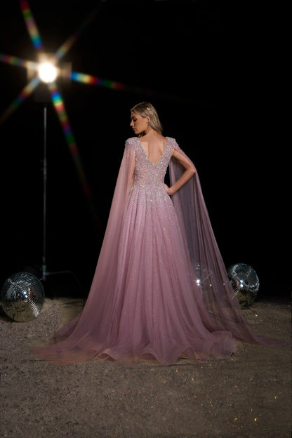 Woman in a pink evening gown with a cape against a dark background